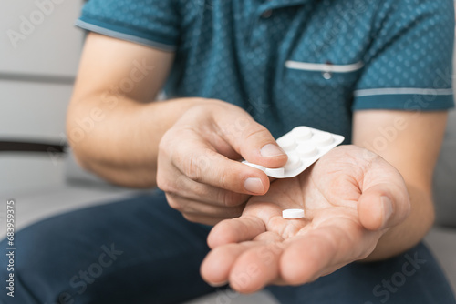 Man taking medicine from blister pack  holding white therapeutic pill  antibiotic  painkiller in a hand  close-up view