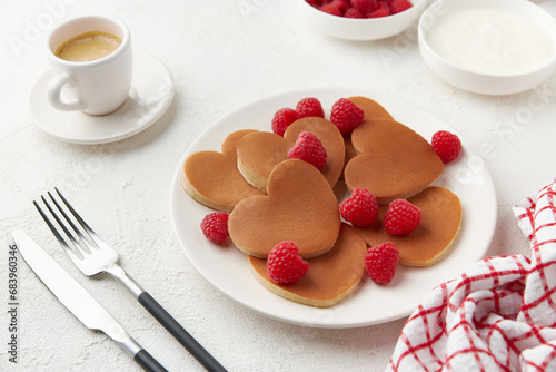 A heap of heart shaped pancakes on the white plate with raspberries on the white background