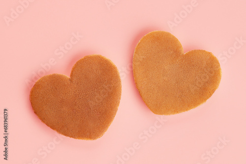 Close up top view of two heart shaped pancakes on the pink background