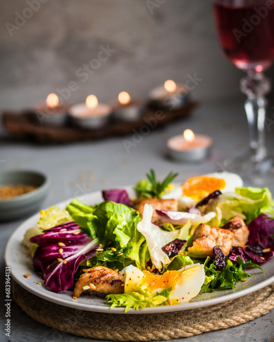 A bowl of salad with a mix of lettuce, chicken, parmesan cheese and other ingredients in a romantic setting with a glass of rose wine.