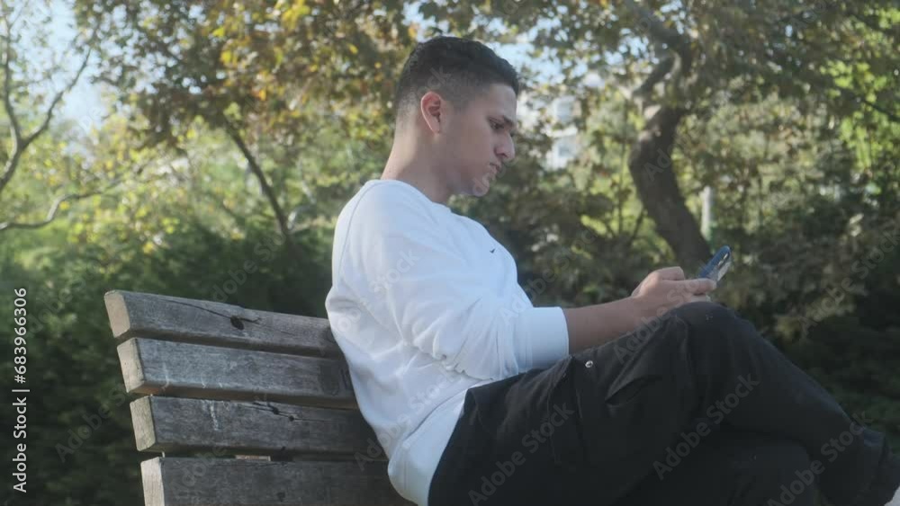 Man sitting on park bench looking at his phone, Man sitting on park bench looking at his phone,