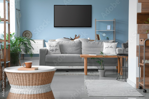 Modern smart TV set hanging on blue wall in living room