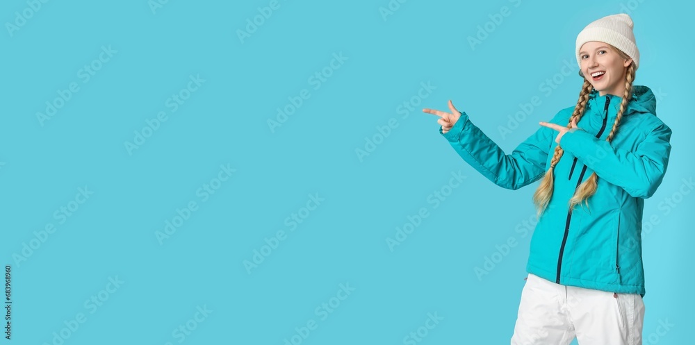 Pretty young girl in warm winter clothes pointing at something on light blue background with space for text Pretty young girl in warm winter clothes pointing at something on light blue background with space for text