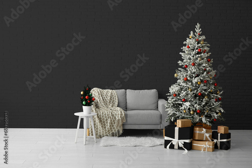 Beautiful Christmas tree with gifts and comfortable sofa near dark wall. Banner for design photo