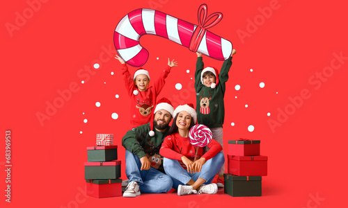 Fotografia Happy family in Santa hats, with Christmas gifts and candies on red background