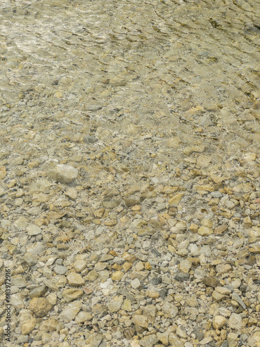 Traquil abstract background of pebbles under clear water. Ripple on a water surface. Beige color. Vertical format.