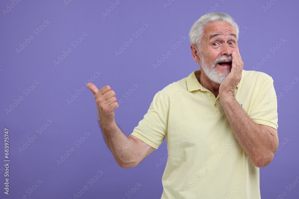 Special promotion. Emotional senior man pointing at something on purple background. Space for text Special promotion. Emotional senior man pointing at something on purple background. Space for text