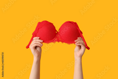 Woman holding sexy re bra on yellow background, closeup photo