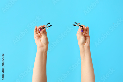 Female hands with nipple clamps from sex shop on color background, closeup photo