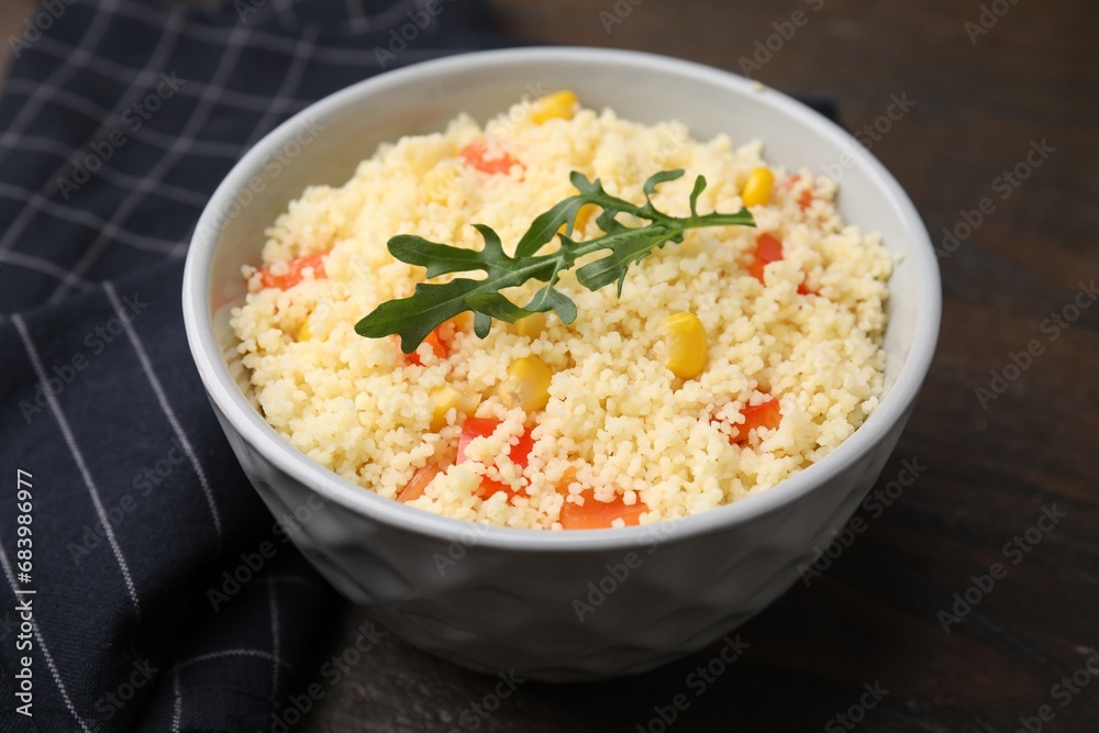 Tasty couscous with pepper, corn and arugula in bowl on wooden table, closeup Tasty couscous with pepper, corn and arugula in bowl on wooden table, closeup