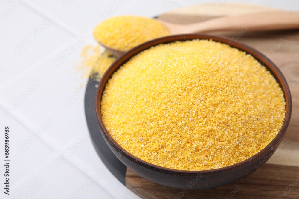 Raw cornmeal in bowl on white tiled table, closeup. Space for text Raw cornmeal in bowl on white tiled table, closeup. Space for text