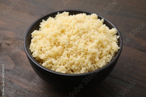 Tasty couscous in bowl on wooden table, closeup