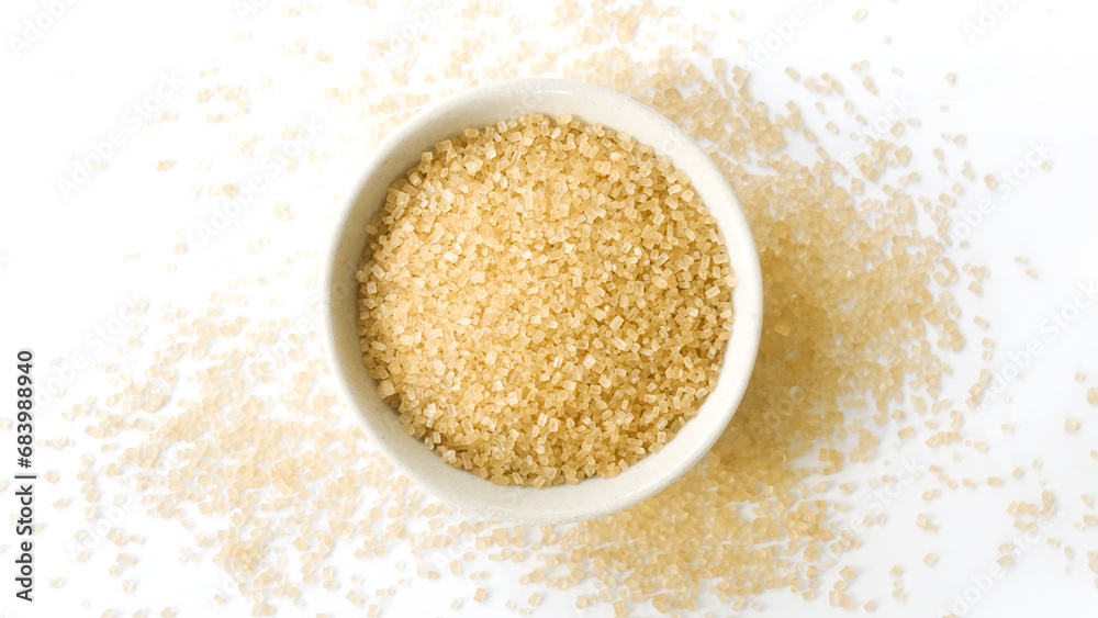 Small bowl of raw brown sugar with scattered crystals on white background Small bowl of raw brown sugar with scattered crystals on white background
