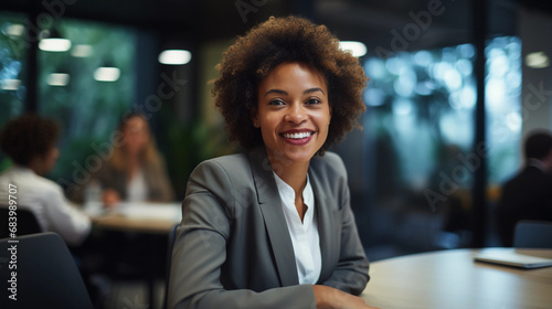 Portrait of a businesswoman. Beautiful black African American woman smiling wearing formal outfit suit in office sitting at desk.