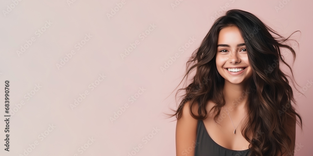 Smimilg young woman with tanned skin and long groomed hair isolated on flat beige pastel background with copy space. Model for banner of cosmetic products, beauty salon and dentistry