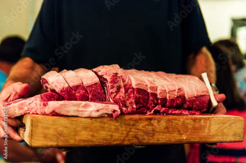A man holds a brown butcher block with cuts of raw ribeye steak  photo
