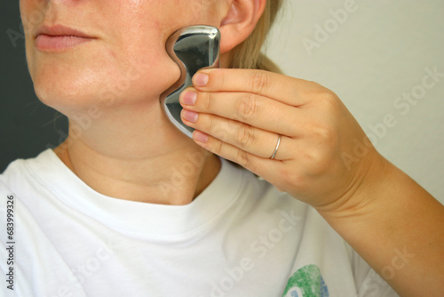 Millennial caucasian woman using a metal gua she tool for lifting the face