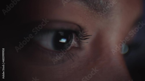 Close-up of young black woman eyes looking at device screen, working with computer laptop. Monitor light is reflected in her face. Female freelancer on Internet at dark night in living room. photo