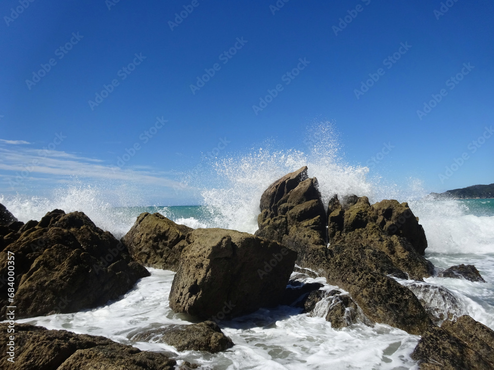 Tosende Welle schlägt gegen Felsen in der Brandung im Meer mit blauem Himmel im Hintergrund