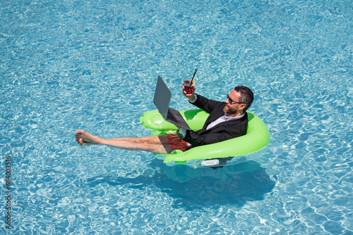 Summer vacations and freedom travel concept. Portrait of hispanic business man on the beach. Businessman in suit floating with laptop and cocktail in pool. Crazy business man dreams summer vacation.