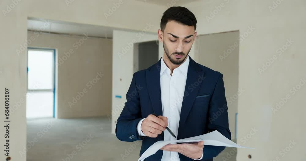 Portrait of successful young man in smart elegant suit holding plan of the building in hands looking in after that explaining layout of the apartment at camera for newpotential clients customers. Portrait of successful young man in smart elegant suit holding plan of the building in hands looking in after that explaining layout of the apartment at camera for newpotential clients customers.