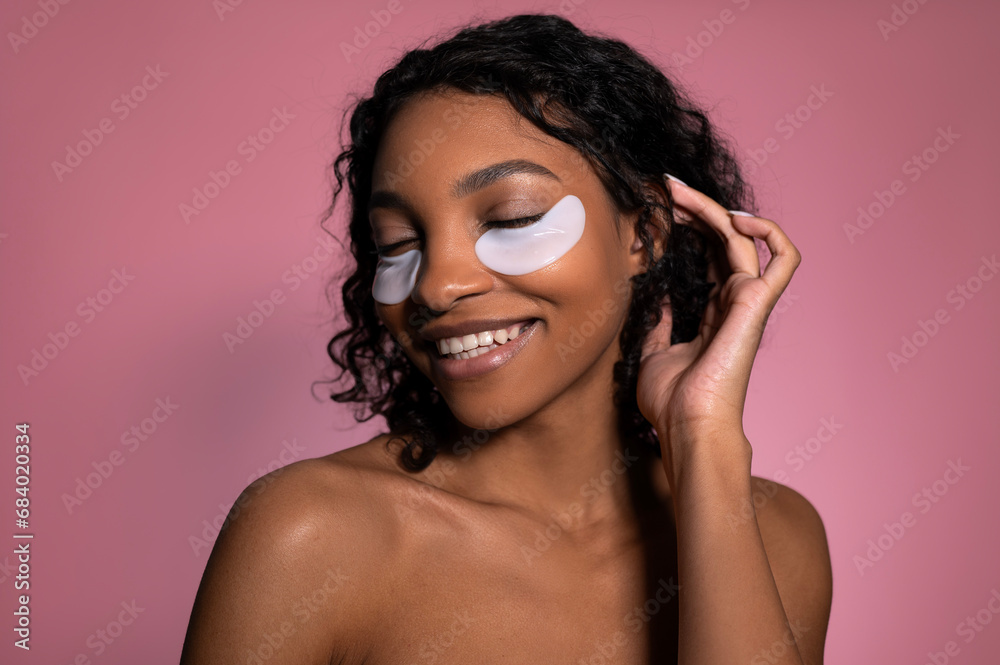Closeup studio shot of smiling happy dark skinned girl with patches under eyes. Beauty and wellness concept Closeup studio shot of smiling happy dark skinned girl with patches under eyes. Beauty and wellness concept