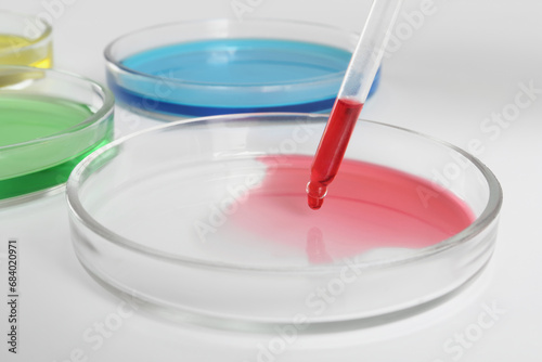 Dripping red liquid into Petri dish on white background, closeup