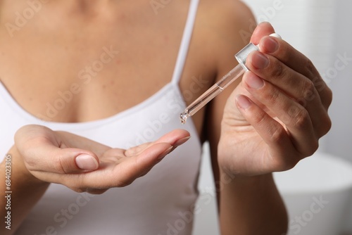 Woman applying cosmetic serum onto her finger on light background  closeup