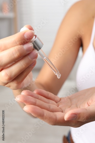 Woman applying cosmetic serum onto her hand on blurred background, closeup