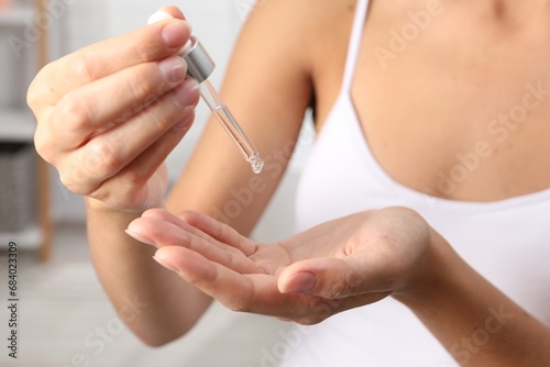 Woman applying cosmetic serum onto her hand on blurred background  closeup