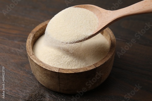 Pouring uncooked organic semolina into bowl on wooden table, closeup photo