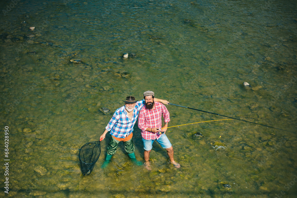 Two men friends fisherman fishing on river. Old father and son with rod fishing at riverside. Recreational activity. Water background.