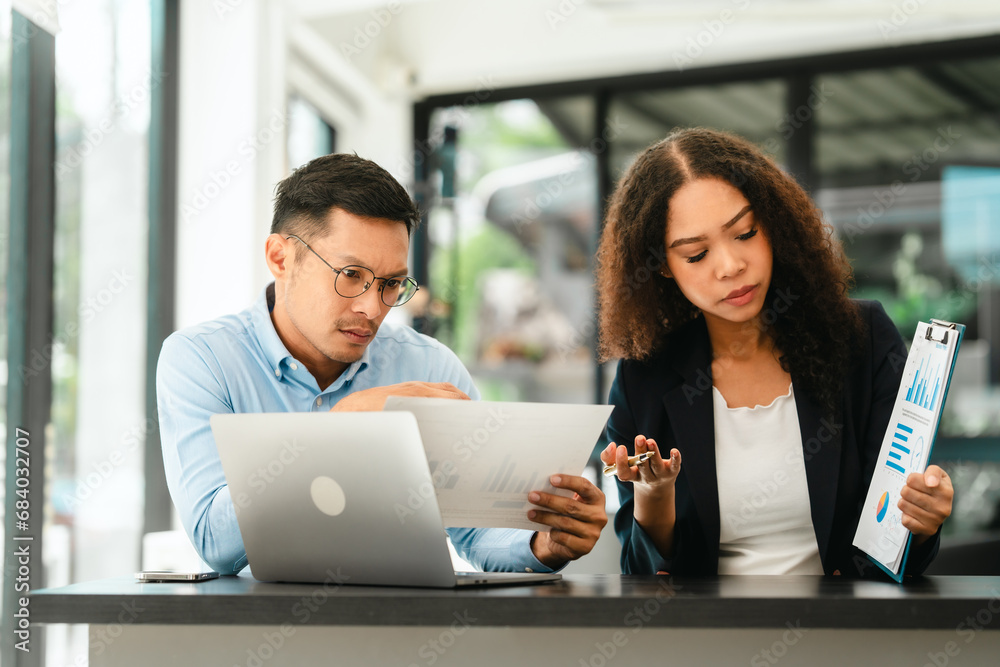Asian business man and African American woman engaging in business discussion, possibly about merger or joint venture. two companies become one, one of companies often survives while other disappears Asian business man and African American woman engaging in business discussion, possibly about merger or joint venture. two companies become one, one of companies often survives while other disappears