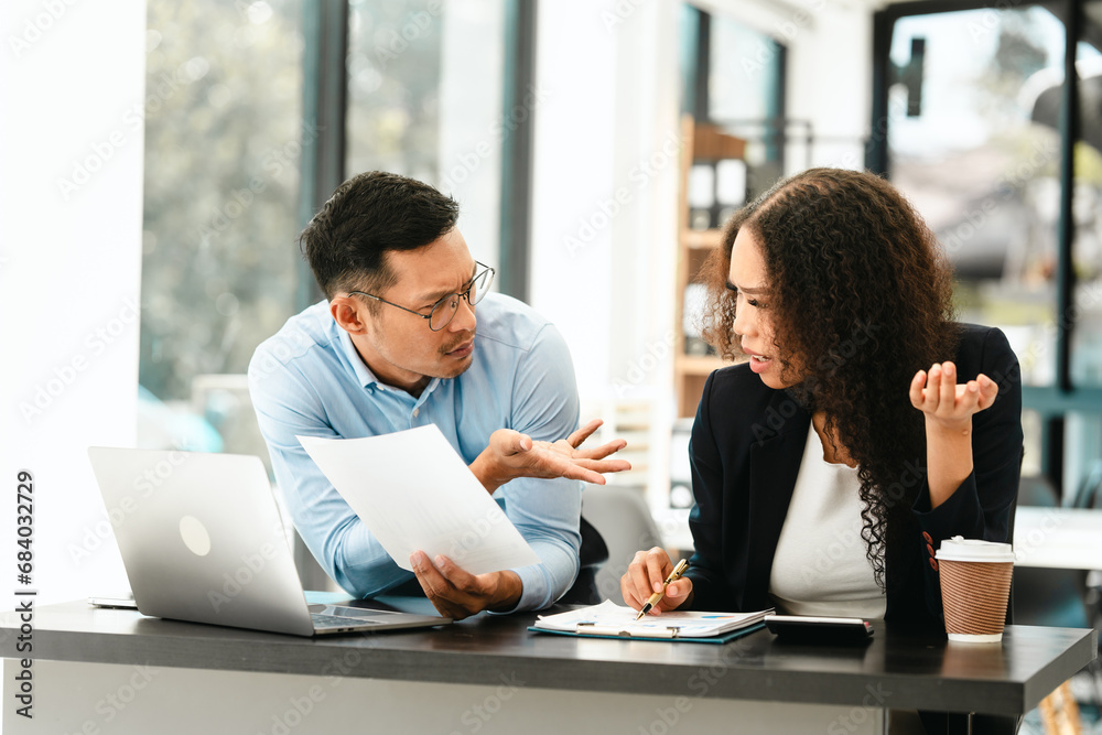 Asian business man and African American woman engaging in business discussion, possibly about merger or joint venture. two companies become one, one of companies often survives while other disappears Asian business man and African American woman engaging in business discussion, possibly about merger or joint venture. two companies become one, one of companies often survives while other disappears