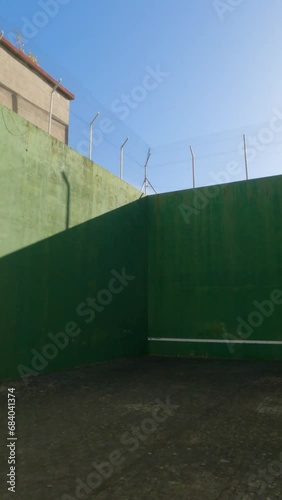 Wallpaper Mural Explore the dynamic ambiance of a concrete-floored court wall, camera gliding towards the towering dark green walls adorned with a low white horizontal line. Shadowed elegance under a clear, blue sky. Torontodigital.ca