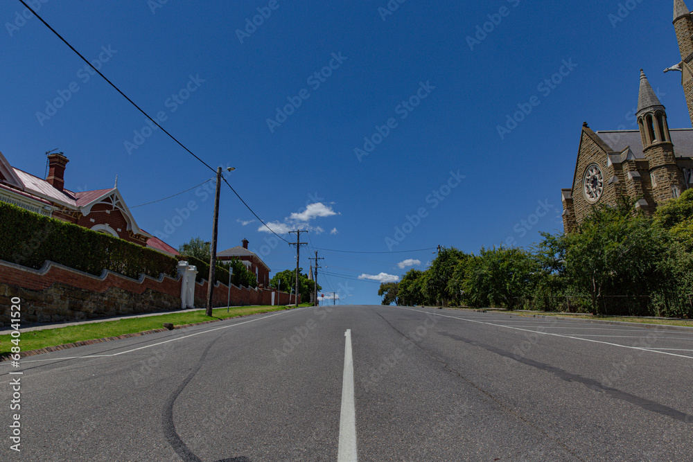 Quiet Street Perspective with Vintage Church and Brick Houses Under Blue Sky