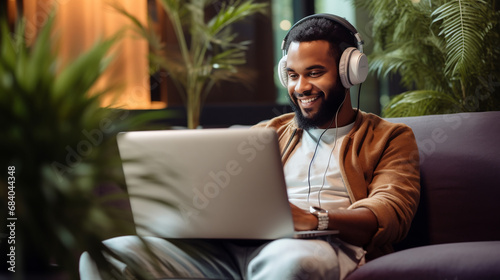 Young smiling afro male working on laptop. Man wearing headphones for listen music and sitting puffs. photo