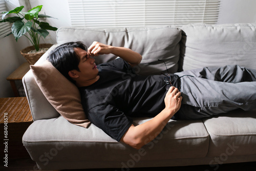 Man with mental health problem lying on the couch with exhausted and using hand to massage nose
