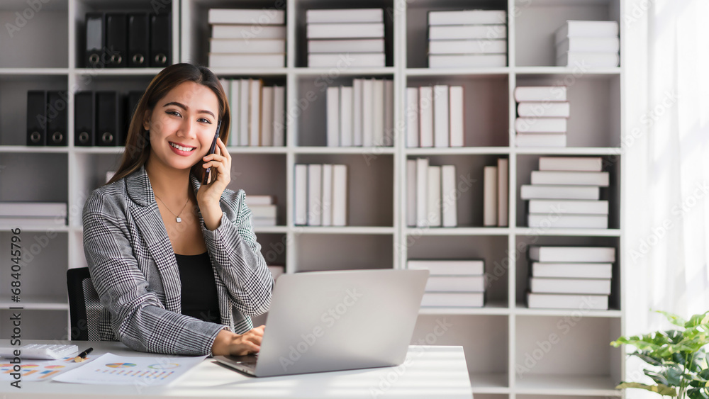 Businesswoman checking business data to typing on laptop and talking with colleague on smartphone Businesswoman checking business data to typing on laptop and talking with colleague on smartphone