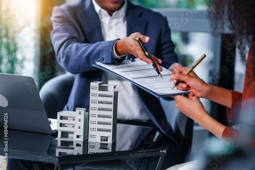 Attractive Asian businessman and African American female real estate and land investor talk discussing together on table with laptop and small building model. Reserve fund.
