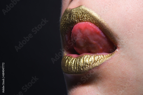 Sexy tongue licking lips. Golden lips. Luxury gold lips make-up. Golden lips with creative metallic lipstick. Gold metal lip. Sensual woman mouth, clse up, macro. photo