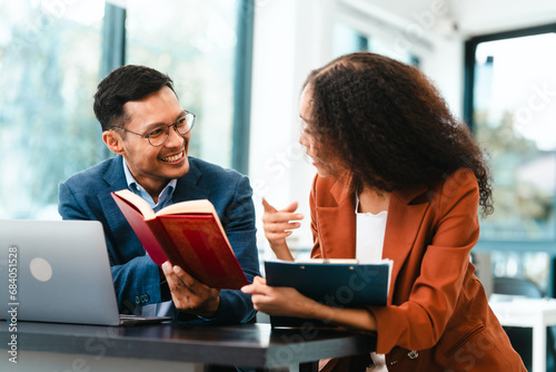 Attractive Asian businessman and an African American businesswoman, both in formal suits, intently review a contract paper together.