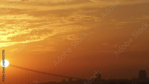 a helicopter is flying towards the sun during sunset-golden hour time. sun is visible through the bridge. golden hour time in Istanbul.