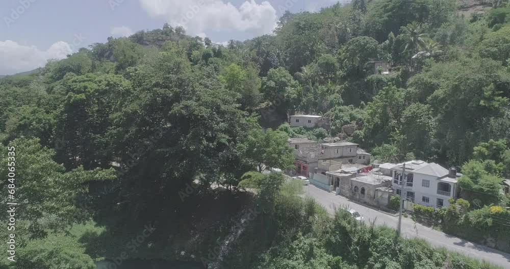 Drone shot around a forested hill with houses under a suny sky