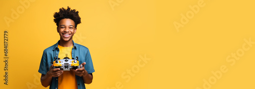 Excited African-American boy look straight into camera with robot in hands on blue studio background. Electric toys learning robots at robotics horizontal studio plain banner copy paste space for text