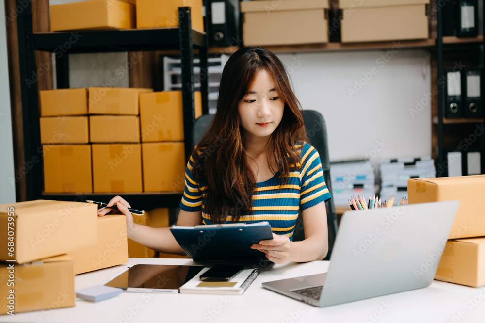 Young business owner woman prepare parcel box and standing check online orders for deliver to customer. Shopping Online concept. Young business owner woman prepare parcel box and standing check online orders for deliver to customer. Shopping Online concept.