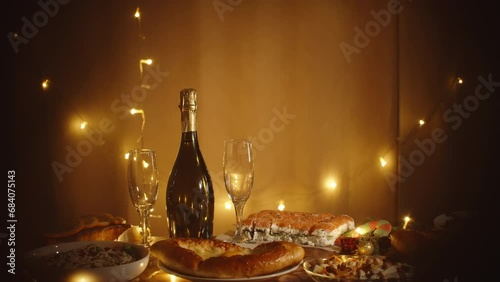 Warm and cozy Christmas ambiance at home, festive table with food and champagne for two, amidst twinkling garlands. Bokeh effect with star-shaped blurs due to focusing technique.