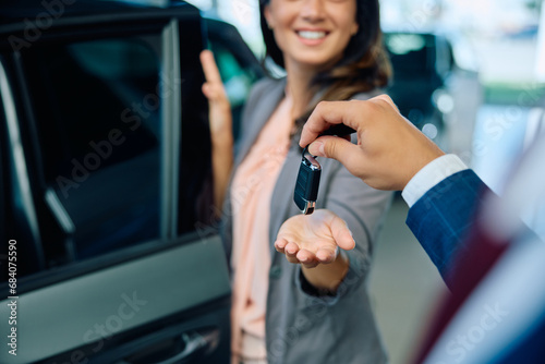 Close up of salesman giving car key to female customer in showroom.