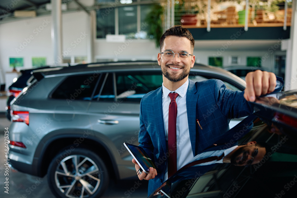 Happy car salesman in showroom looking at camera.