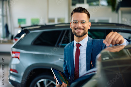 Happy salesman working at car dealership and looking at camera. © Drazen